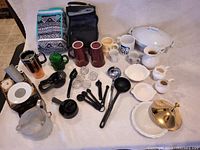 Photo showing full spread of kitchenware items on white surface, including mugs, serving dishes, utensils, and bags