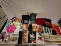 Overview of miscellaneous household items including books, headphones, blanket, and small accessories laid out on a beige cloth backdrop.