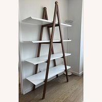 Front view of white and walnut ladder bookshelf against wall