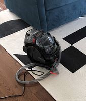 Side view of Bissell SpotClean Pro carpet cleaner with attached hose and power cord on floor.