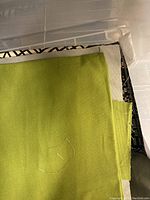 Various fabric remnants stacked in plastic bin, showing solid olive and green canvas pieces and geometric pattern upholstery samples