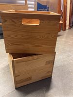 Two solid wood IKEA storage boxes stacked, showing an outside view of the wood boxes with visible grain and cut-out handles.