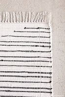 Close-up image of the Urban Outfitters white with black stripe rag rug showing woven design and fringed edges.