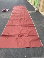 Long maroon vinyl-coated cotton canvas fabric laid out on asphalt showing length and texture for outdoor upholstery or bags.