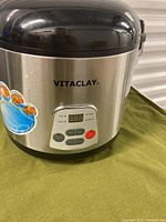 Front view of VitaClay slow cooker showing stainless steel body, control panel with digital display and buttons, and black lid.