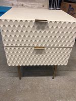 Front view showing textured geometric pattern on two drawers with antique brass handles and metal legs.