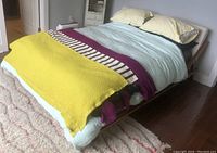 Queen size bed setup with CB2 Drommen acacia wood frame and ivory upholstered headboard, showing bedding and mattress on wood floor.