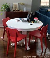 Full view of the white round dining table with four red chairs around it in a living space, showing the pedestal base and tabletop.