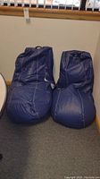 Two blue bean bag chairs placed side by side, showing overall size and shape leaning against wall.