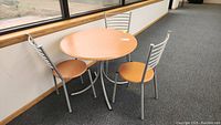 Photo showing round bistro table with wood-look surface and three matching chairs with metal frames and wood seats.