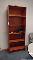 Front view of the five shelf wooden bookcase with some small office items on shelves.