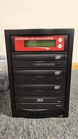 Front view of the Kanguru CD duplicator showing the red LCD control panel and four optical drives.