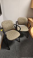 Two matching office chairs with patterned upholstery and black metal armrests/legs.