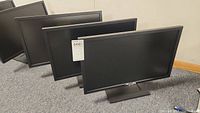 Three 23-inch Dell monitors arranged in a row on carpeted floor, angled to show front and sides, all with stands attached.