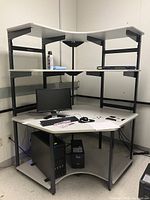 Front and side view of white laminated three tiered corner desk with black metal frame showing monitor, keyboard, and computer tower placed on desk and floor