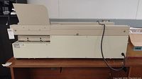 Side view of beige Duplo Perfect Binder electric binding machine on tabletop showing overall shape and power cord.