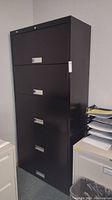 Front view of the black HON lateral file cabinet showing all five drawers with horizontal silver handles and key lock on top drawer.