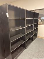 Photo showing three black metal shelving units lined up side by side with multiple shelves each.