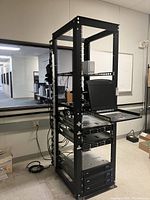 Three-quarter front view showing open-frame rack loaded with sliding keyboard tray, UPS modules and cabling.