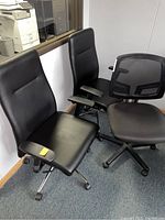 Photo showing two black leather-like high-back office chairs with padded armrests and one black mesh low-back office chair, all with pneumatic adjustments and wheels in office setting.