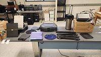 Overview of tabletop showing multiple black mouse pads, blue folders, black document holders, stainless steel coffee pot, and boxed Xerox DocuMate scanner.