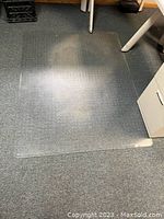 Clear rectangular office chair mat placed on carpet with visible floor texture underneath.