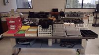 Full view of the office supplies lot on a grey table in a well-lit room, showing folders, document holders, trays, magazine holders, and other desk organizers.