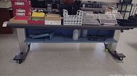 Wide view showing the full table with items on the surface and shelf below. Includes multiple boxes and trays for workspace storage.