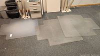 Three clear plastic chair mats laid overlapping on carpeted floor, showing sizes and shapes including cutouts for desk placement.