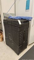 Full view of closed black plastic tradeshow display case with side handle and wheels, blue item on top.