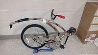 Full view of Trail-A-Bike tandem trailer bike attachment with metallic silver frame, red and black decals, black padded seat, handlebar with red grips, and single rear knobby tire.