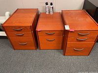 Three cherry-stained wood file cabinets placed side by side on carpeted floor with spray cans on top of two cabinets.