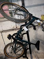 Photo of entire bike showing green frame, 19-inch rugged tires with yellow sidewalls, and visible dirt and flat tires; bike is hanging on a wall in a basement.
