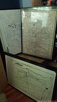 Three framed vintage maps leaning against a bookshelf and wall, two showing Montclair and one East Chicago detail