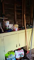 Full view of assortment of garden tools and lawn care items on and above a yellow cabinet inside garage