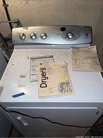 Front view of the GE Profile clothes dryer with instruction manuals on top of the machine