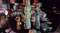 Wide view of the lot displaying the Lladro figurine, Asian figure, Disney Pinocchio figure, and coasters on a table.