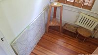 Photo showing marble slab leaning against wall with wooden planter stand and two wooden stools in corner on wooden floor.
