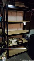 Full front view of black metal shelving unit with four wood composite shelves, some items on lowest shelf.
