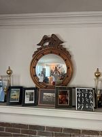 Photo of the circular mirror with bronze frame and bird design above it, mounted on the wall above several framed pictures.