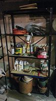 Two black metal shelving units with shelves adjustable in height. Dust and some pitting visible from humidity exposure. Various items on shelves not included.