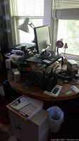 The photo shows a round wooden table cluttered with a black LG monitor, white desk lamp, smaller pink lamp, tangled computer cables, and other computer accessories.