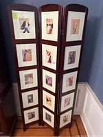 Full view of the wooden room divider with three folds and multiple glass picture frames with vintage art prints.