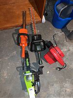 Lot items: Green Poulenc chainsaw, two hedge trimmers (orange and green), red electric garden tool on floor