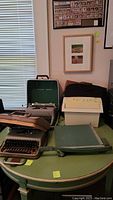 Photo of vintage Olivetti and Royal typewriters with cases, shredders, paper cutter, and briefcases