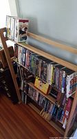 Wooden shelves filled with numerous VHS tapes and some DVD cases, visible titles on the spines vary.