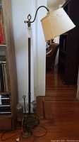 Full view of tall vintage floor lamp with adjustable arm and beige shade standing on wooden floor next to furniture.