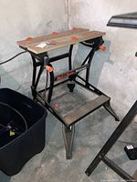 Black & Decker Workmate bench with wood top and metal frame shown from side angle in basement.