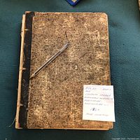 Front cover of The Canadian Farmer journal, showing worn marbled cover with black spine; pen placed on top and note indicating 1864 publication and poor condition