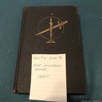 Closed hardcover book titled 'The Mystery Book' with a black cover featuring a gold embossed candle and dagger. A note indicates the book may be from 1934.